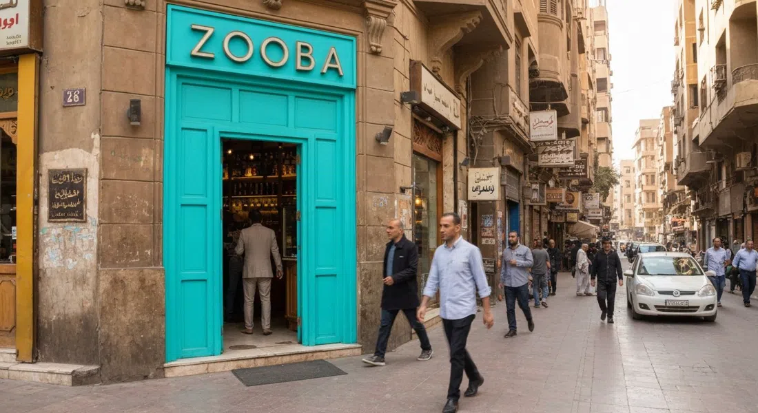 La puerta turquesa brillante de Zooba en la calle 26 de Julio, con la entrada enmarcada por el tráfico peatonal de El Cairo y la sombra de la tarde